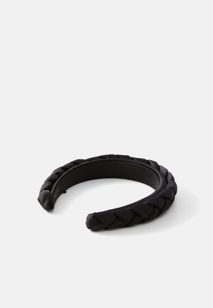 Diadema trenzada negra hecha de un material suave, con un diseño de banda gruesa con bordes redondeados y un patrón trenzado texturizado.