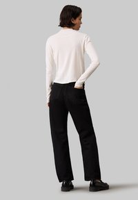 Jean noir à jambe droite avec poches arrière, associé à un haut crème à manches longues. Le tissu semble doux ; le design est minimal avec une légère taille.