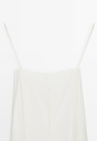 Weißes Kleid mit dünnen Trägern, geradem Ausschnitt und vertikalen Nähten. Sanfte Stofftextur, bodenlanger Schnitt mit einem einfachen, minimalistischen Look.