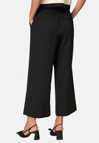 Pantalons larges noirs avec une taille élastique, dotés de deux poches au dos. Fabriqués en tissu lisse et léger.