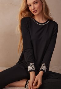 Schwarzes Loungewear-Set bestehend aus einem Langarmoberteil mit einem weißen Ausschnitt und Spitzenakzenten an den Bündchen, kombiniert mit passenden, engen Hosen.