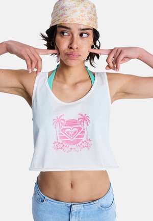 Jeune femme portant un foulard fleuri, un débardeur blanc avec un motif de palmier rose, et un jean bleu, pressant ses index contre ses oreilles.