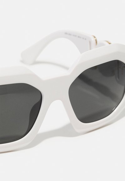 White hexagonal sunglasses with dark gray lenses, featuring thick frames and smooth, glossy texture. Gold accents near the temple.