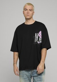 Černé oversized tričko z bavlny s růžovým grafickým motivem na hrudi, doplněné světle modrými džíny s distressed efektem.