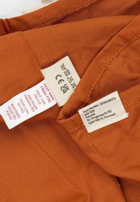 Bruine stof met een gladde textuur, met meerdere waslabels waaronder wasinstructies en een stijlnummer.