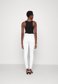 Top preto sem mangas com uma textura suave, combinado com calças brancas ajustadas. As calças brancas apresentam bolsos traseiros e uma bainha ligeiramente cropped.