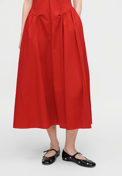 Κόκκινο φόρεμα μήκους μέχρι το γόνατο με ραμμένες πλευρές και απαλή υφή. Μαύρες μπαλαρίνες με κυκλικά ανοίγματα και λουράκι στον αστράγαλο.