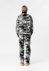 Conjunto de chaqueta y pantalones patroneados en blanco y negro, fabricado con tejido texturizado; presenta un collar y un detalle de etiqueta en la parte posterior.