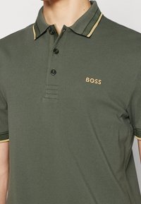 Grön polo skjorta med texturerad tyg, med en tvåknapps-knäppning, kontrasterande krage och guld "BOSS" logotyp på bröstet.