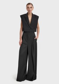 Czarna dopasowana, krótka marynarka z szerokimi ramionami, zapinana na pojedynczy guzik, w połączeniu z spodniami o wysokim stanie z zakładkami i szerokimi nogawkami.