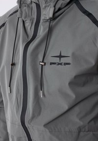 Giacca grigia con cappuccio, zip frontale e cordini regolabili con accenti metallici. Include un logo nero sul petto.