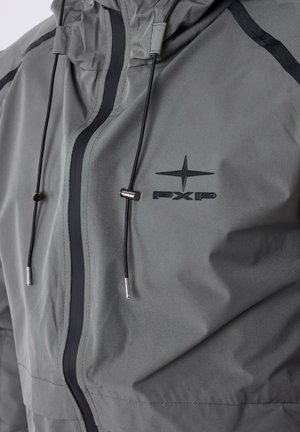 Chaqueta gris con capucha, cierre frontal y cordones ajustables con detalles metálicos. Incluye un logo negro en el pecho.