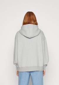Gray hooded sweatshirt made of soft fabric, featuring a loose fit and ribbed cuffs. Back view shows a large hood and subtle seam details.