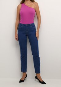 Top de tirantes ajustado de canalé en un vibrante rosa, con diseño de un solo hombro, combinado con pantalones vaqueros de tiro alto en azul y tacones negros de punta.