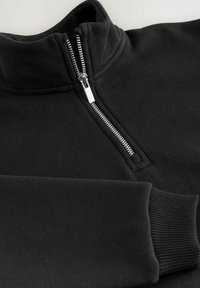 Sudadera de forro polar negro con cuello alto y cremallera plateada. Presenta puños acanalados y una textura suave. Diseño simple y minimalista.