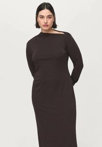 Lange, aansluitende donkerbruine jurk met lange mouwen, voorzien van een asymmetrische halslijn en een gladde textuur. Eenvoudig, elegant ontwerp.