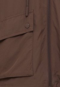 Brązowa wodoodporna tkanina kurtki z boczną kieszenią, zapięciem na zatrzaski i przednim zamkiem błyskawicznym. Gładka faktura o matowym wykończeniu.