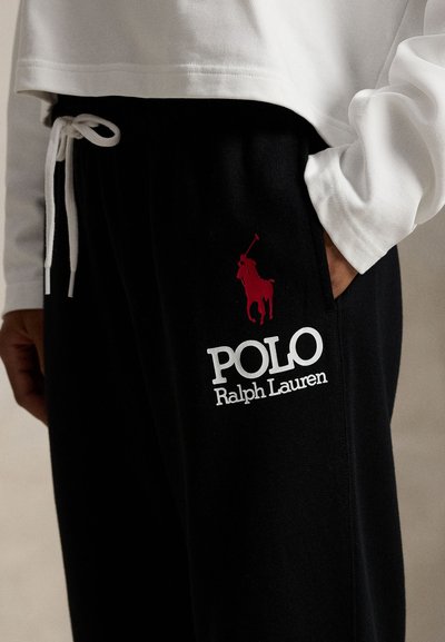 Melnas sporta bikses ar sarkanu polo spēlētāja logo un baltiem "POLO Ralph Lauren" uzrakstiem, ar elastīgu jostas vietu un sānu kabatām.