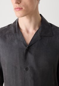 Camisa negra de manga corta hecha de un tejido texturizado, con cuello esparcido, cierre de un solo botón y un brillo sutil.