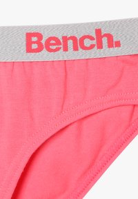 Rózsaszín pamut bugyi szürke gumiszalaggal, amelyen piros betűkkel szerepel a "Bench." felirat. Simább textúra és varrott szélek.