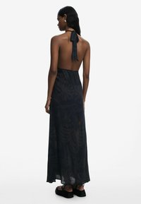 A long, dark patterned dress with a halter neck and open back. Made of lightweight, semi-translucent fabric, gathered at the waist.