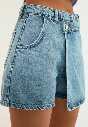 Denim shorts in light blue with a raw hem and front flap detail. Features pockets and a high-waisted design with visible stitching.