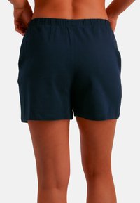 Laivastonsiniset puuvillashortsit, joissa on joustava vyötärönauha, yksinkertainen malli ja reisien puoliväliin ulottuva pituus, korostaen sileää tekstuuria.