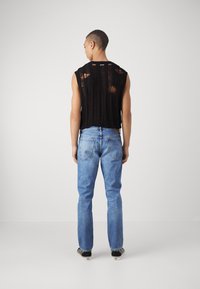 Top senza maniche nero con strisce orizzontali usurate, abbinato a jeans a gamba dritta azzurri e sneakers nere con motivo.