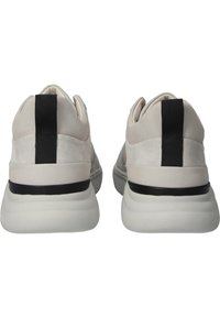 Paire de baskets beige clair avec des semelles blanches épaisses et des rayures verticales noires à l'arrière, vue de dos sur fond blanc.