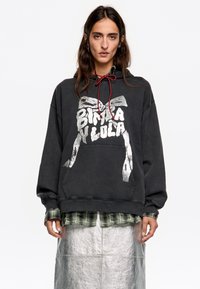 Melna kapuce ar sudraba grafiku un sarkano auklu. Valkāta virs zaļas šūnveida krekla, apvienota ar sudraba metālisku svārku.