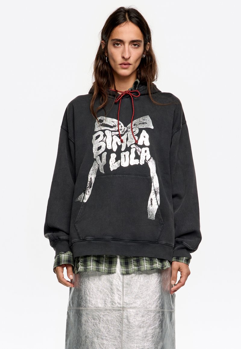 Melna kapuce ar sudraba grafiku un sarkano auklu. Valkāta virs zaļas šūnveida krekla, apvienota ar sudraba metālisku svārku.