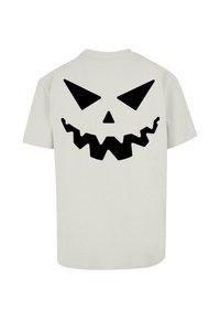 Lysegrå t-shirt med et stort sort græskaransigt grafisk tryk på ryggen, udstyret med spidse øjne og et takkede smil. Korte ærmer, standard pasform.