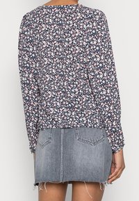 Blusa floreale color blu navy con motivi rosa e bianchi, maniche lunghe, polsini arricciati, abbinata a una gonna di jeans sfilacciata.