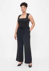 Μαύρο αμάνικο bodysuit με τετράγωνη λαιμόκοψη, σε συνδυασμό με χαλαρούς μαύρους παντελόνες και μαύρες μυτερές γόβες. Απλός σχεδιασμός, λεία υφή.