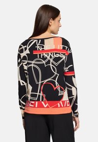 Czarny top z długim rękawem, ozdobiony abstrakcyjnymi wzorami w kolorze kremowym, pomarańczowym i czerwonym oraz napisem. Wykończony kontrastową czerwoną lamówką na dole.