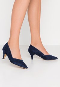 Chaussures à talons hauts en daim bleu marine avec un bout pointu et un design incurvé bas. Caractérisées par un talon de 5 cm et une texture lisse.