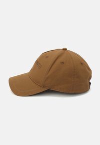 Brown cotton baseball cap with a curved brim, stitched accents, and logo detail on the front. Adjustable strap at the back.