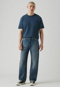 T-shirt in cotone blu navy con maniche corte e scollo rotondo, abbinata a jeans larghi di colore azzurro e sneakers basse bianco e nere.