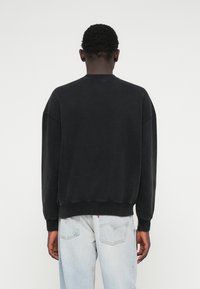 Černá bavlněná mikina s padlými rameny, žebrovanými manžetami a lemem. Vypadá mírně vybledle s měkkou texturou, zobrazeno zezadu.