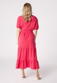 Robe maxi rose à volants avec des manches courtes bouffantes et une ceinture à la taille. Tissu lisse avec une silhouette fluide et un ourlet à volants.