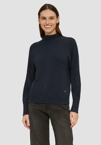 Marineblauer Pullover aus weichem Strickstoff. Hat einen hohen Kragen und eine lockere Passform mit gerippten Bündchen und Saum. Dezente Logodetails am unteren Ende.