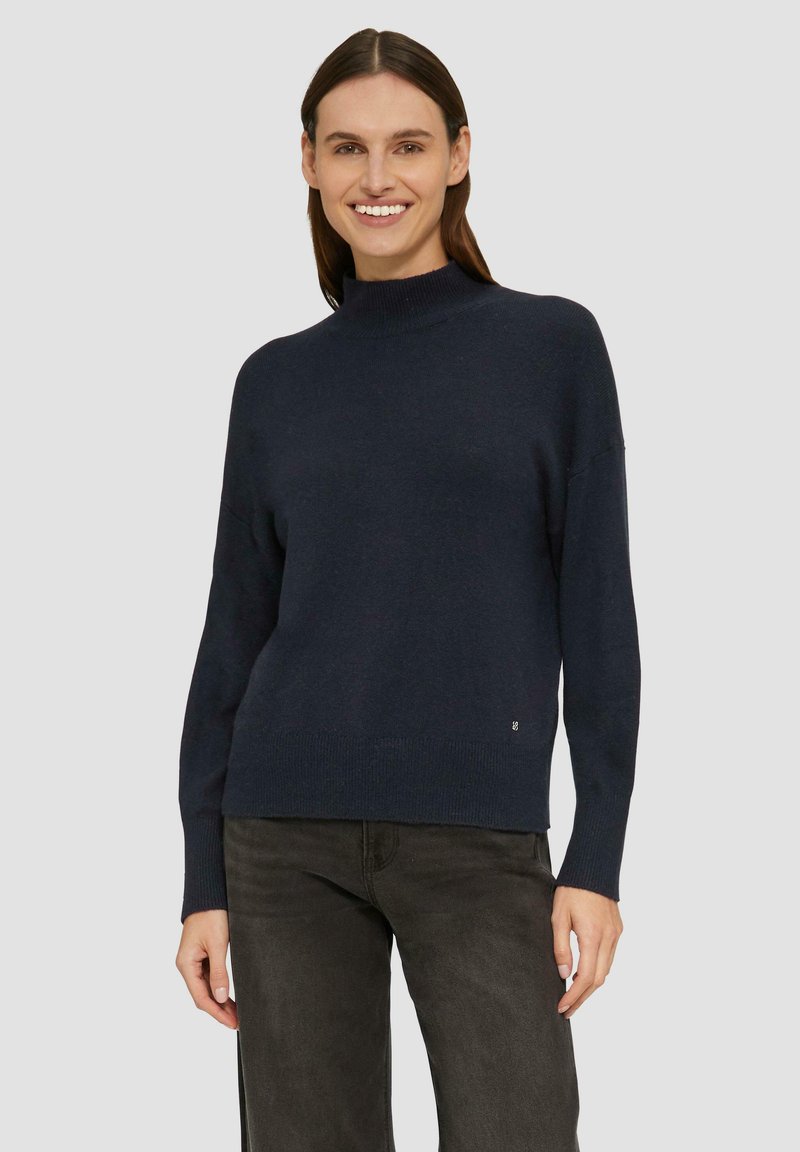 Marineblauer Pullover aus weichem Strickstoff. Hat einen hohen Kragen und eine lockere Passform mit gerippten Bündchen und Saum. Dezente Logodetails am unteren Ende.