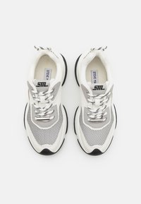 Sneaker bianchi e grigi con pannelli in rete, suola in gomma e accenti neri contrastanti. Presentano il logo e lacci texturizzati.
