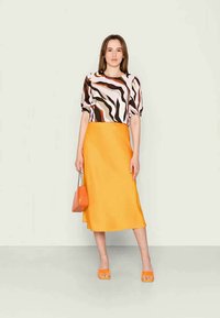 T-shirt de padrão abstrato multicolorido com mangas bufantes, combinado com uma saia midi amarela brilhante e sandálias de salto bloco laranja.