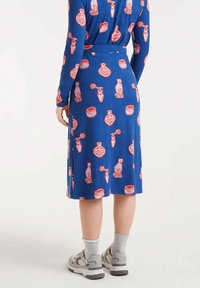 Vestido azul con patrones rojos y blancos de jarrones, gatos y frascos; mangas largas y un cinturón en la cintura; tela suave.