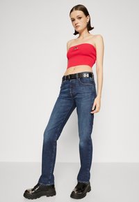 Červený žebrovaný crop top, modré denimové džíny s přiléhavým střihem, černý opasek s oblémi výřezy, černé chunky boty s lesklými akcenty.