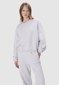 Sweat-shirt gris clair avec une coupe décontractée, poignets et ourlet côtelés, texture douce, porté avec un pantalon de sport assorti, doté de poches latérales.