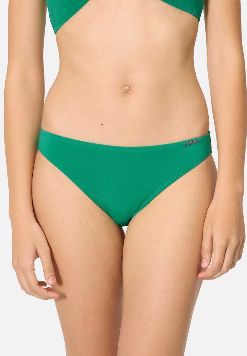 Mujer con bikini verde liso, mostrando desde el abdomen hasta la parte superior de los muslos contra un fondo blanco.