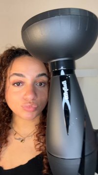 Musta käsikäyttöinen hiustenkuivaaja pyöreällä kulhoilmaventtiilillä. Kahvassa on kiiltävä pinta ja ergonominen muotoilu, jonka korostavat pehmeät kaaret.