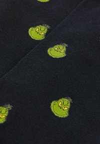 Námořnická tkanina s ribovanou texturou, obsahující opakující se vzory obličejů Grinche v zelené barvě, které zobrazují zlomyslné výrazy a detailní rysy.